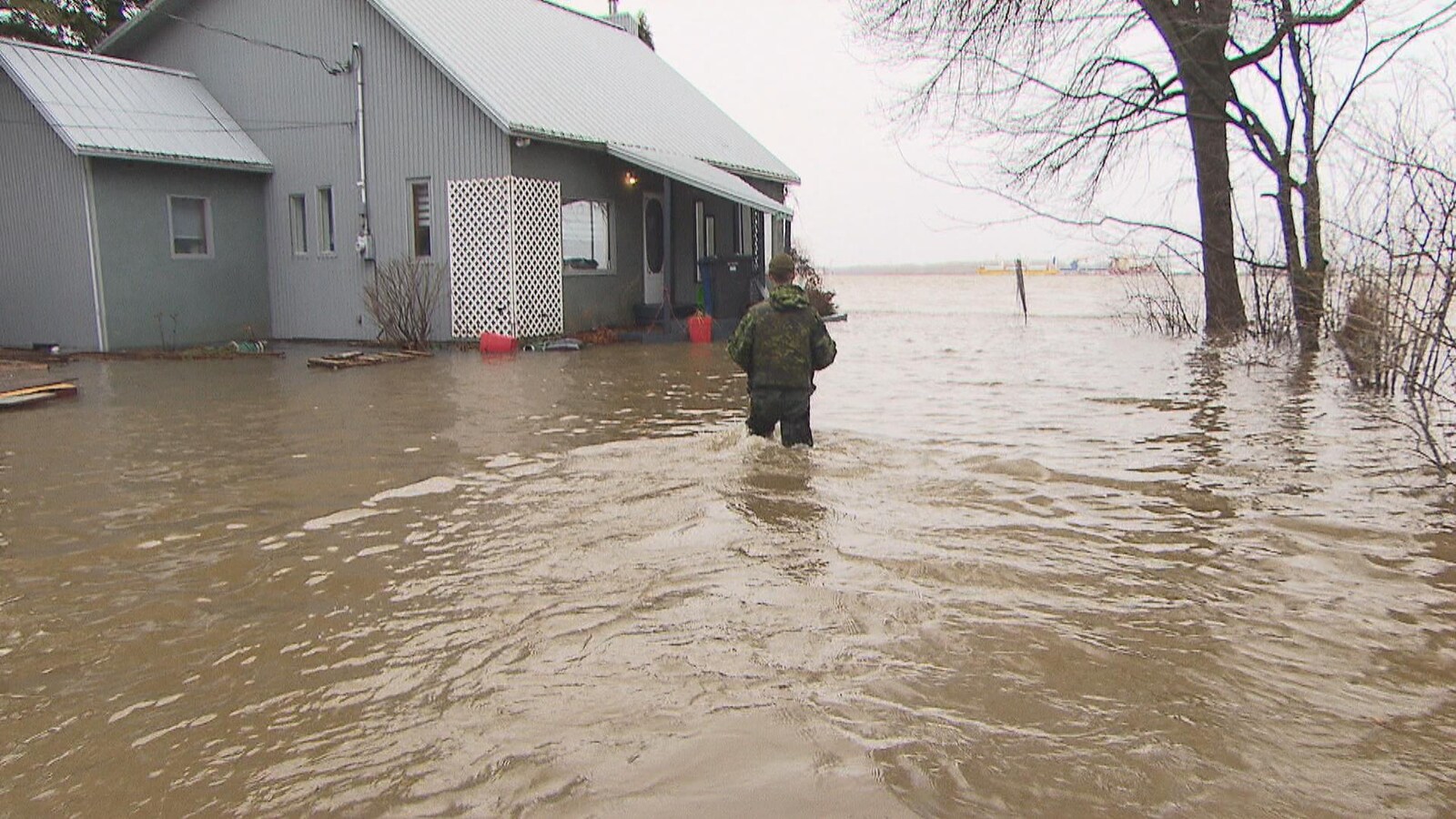 Militaire qui va vers une maison avec de l'eau jusqu'aux cuisses.