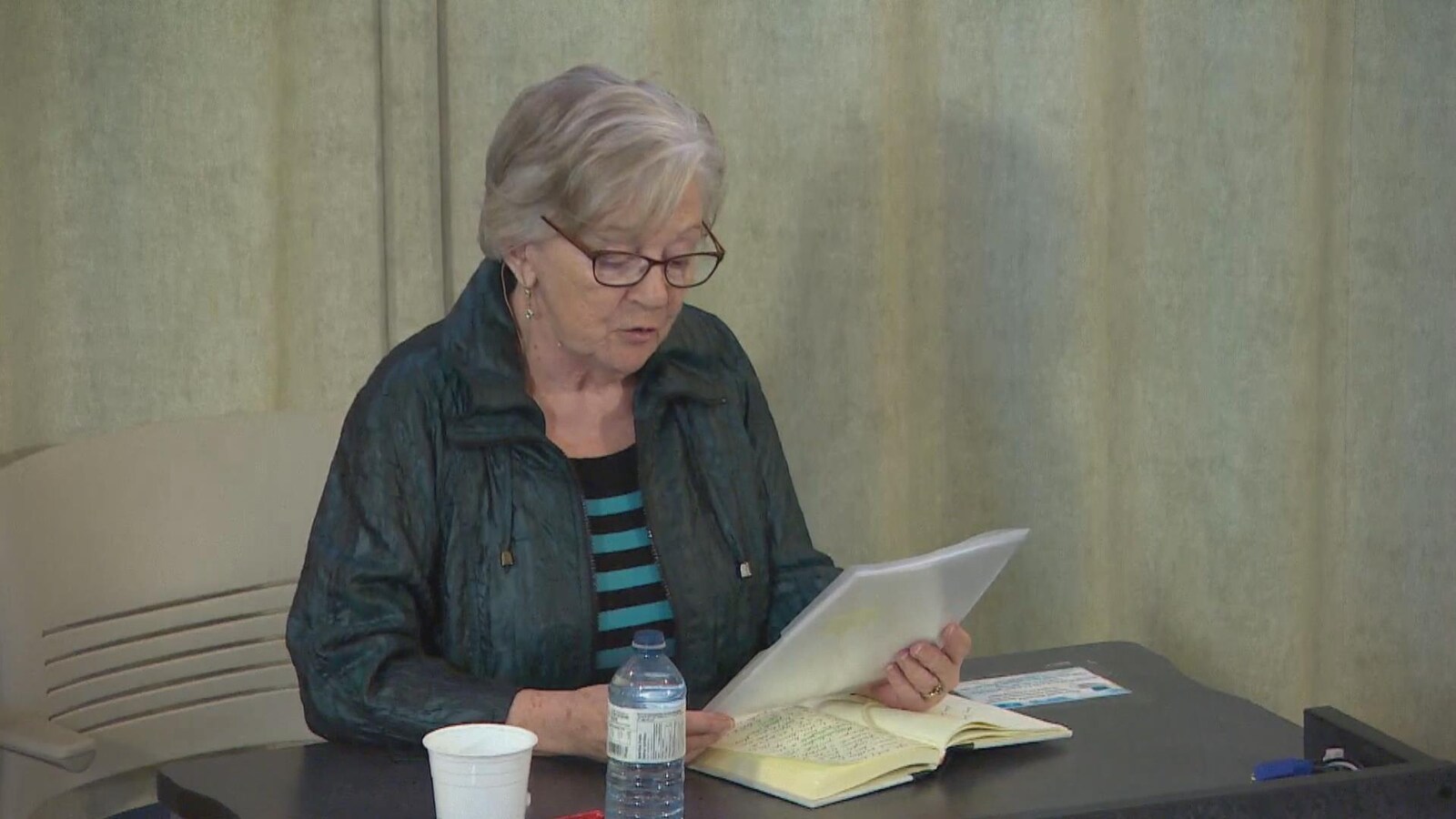 Une femme lit un livre assise à un bureau.