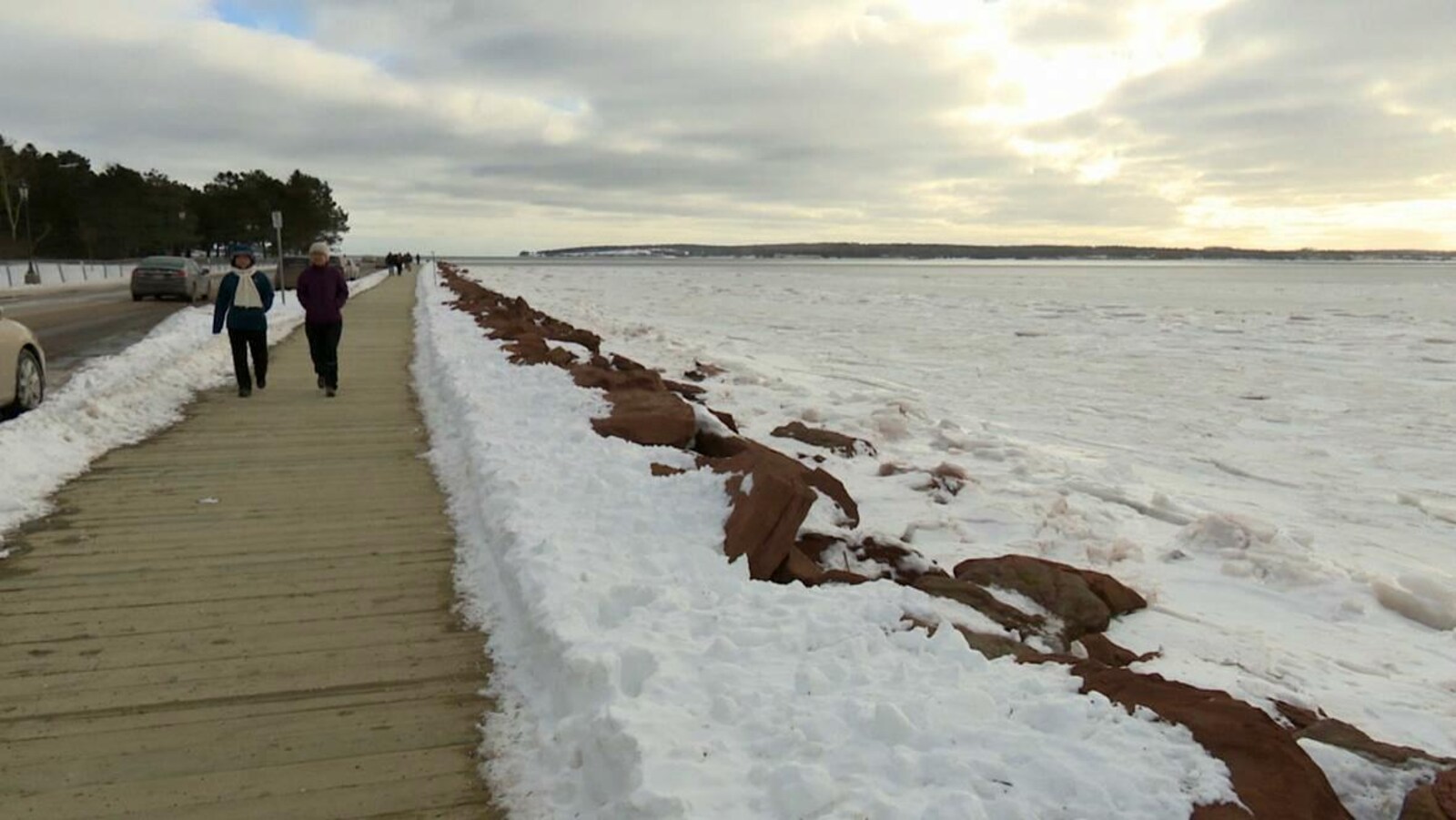 Des gens marchent sur un trottoir de bois bordant la route à deux pas de la mer
