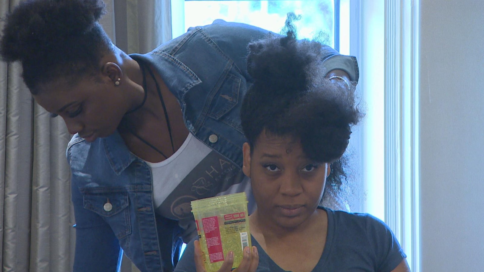 Une jeune femme aux cheveux crépus est assise dans une chaise avec un pot de gel dans la main.