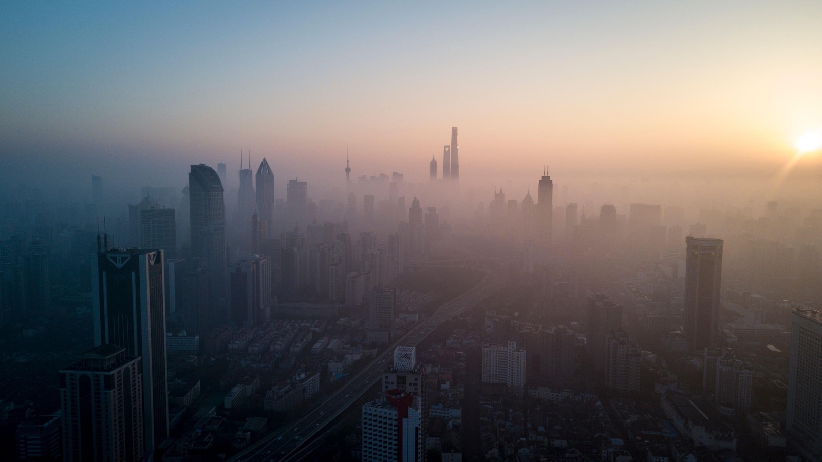 Une ville dont les bâtiments sont embrumés en raison de la pollution est vue de haut et de loin lors du lever du soleil.