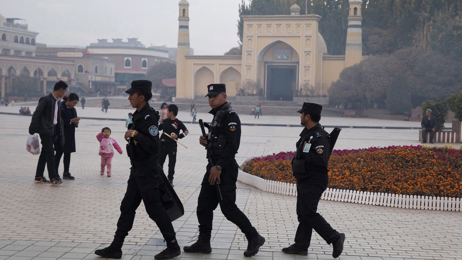 Trois agents de sécurité en uniforme marchent dans un espace public devant une mosquée.