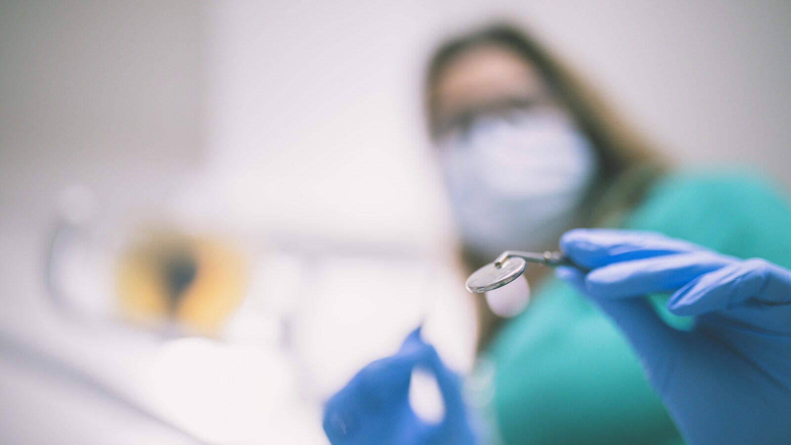 Une femme qui porte un masque de papier devant sa bouche et des gants de plastique tient dans ses mains des outils pour les soins dentaires.