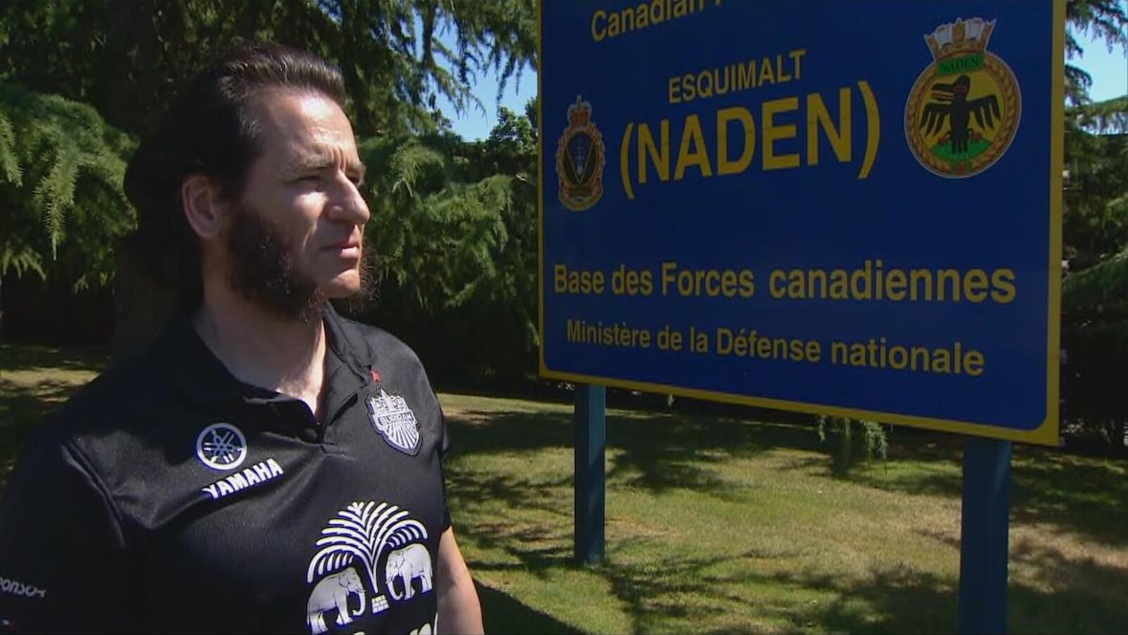 L'homme portant un chandail de sport pose devant le panneau d'entrée de la base militaire.