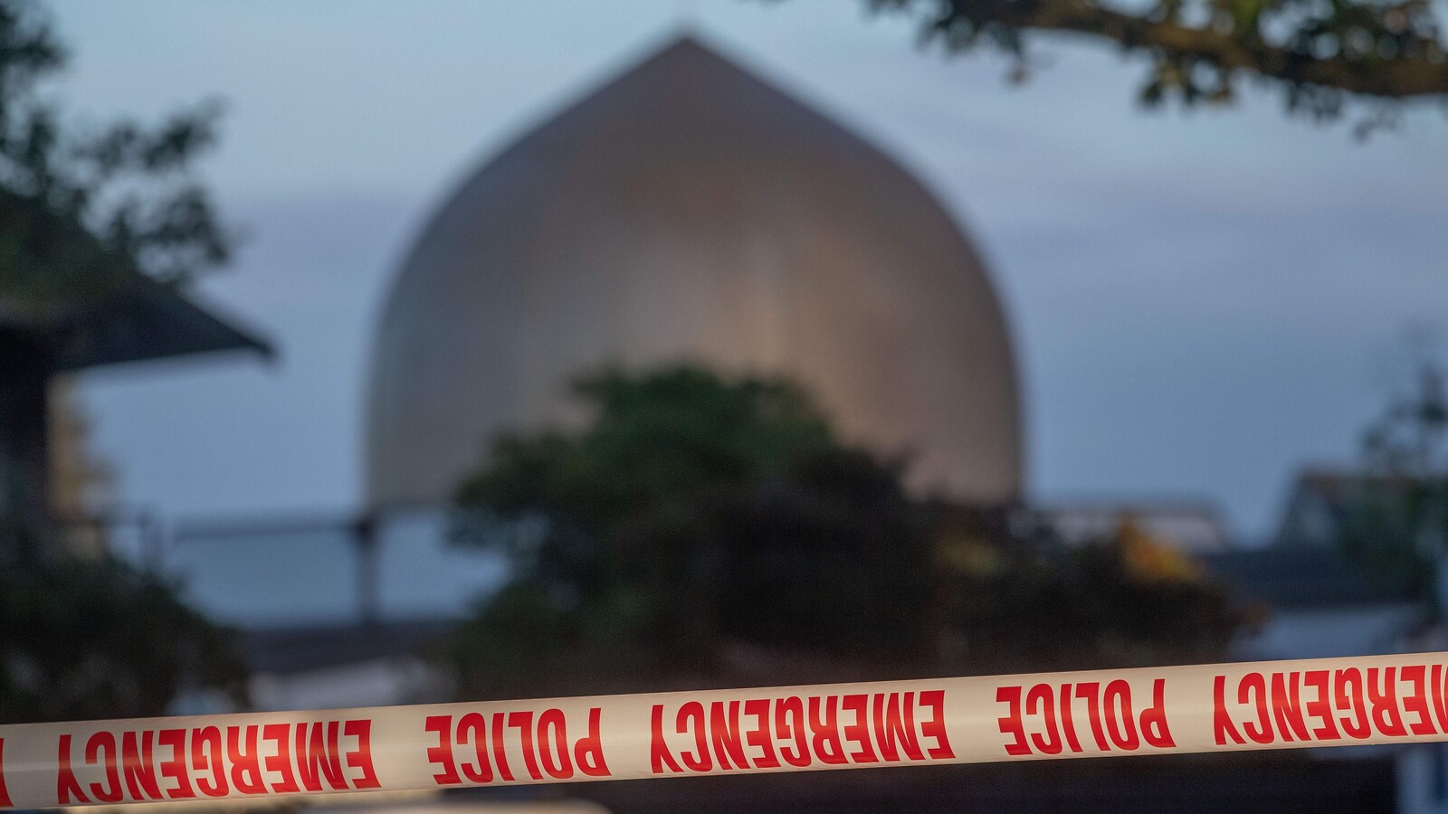 Un cordon de sécurité est visible devant le dôme d'une mosquée entourée d'arbres.