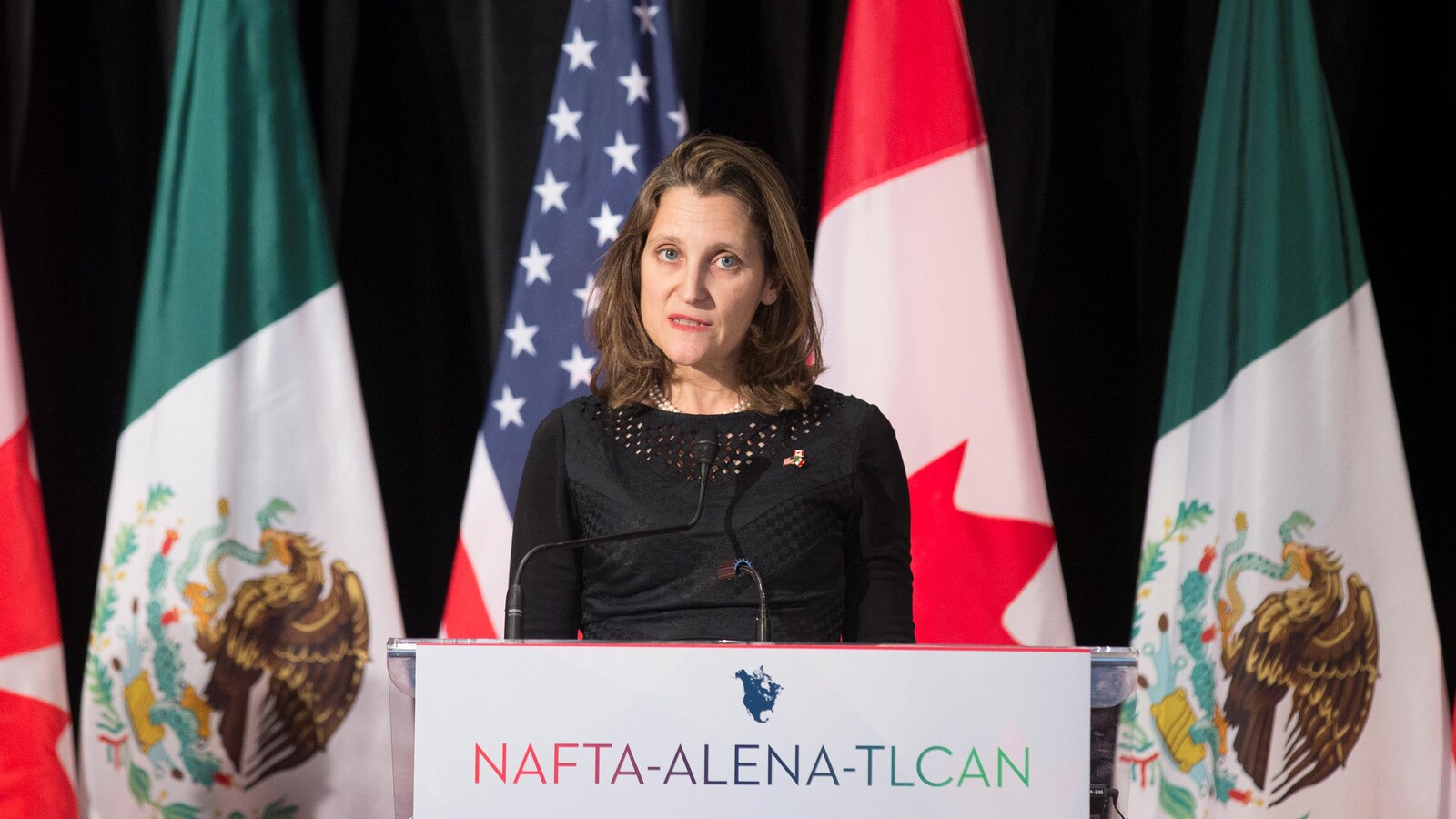 Chrystia Freeland parle devant les drapeaux du Canada, du Mexique et des États-Unis.