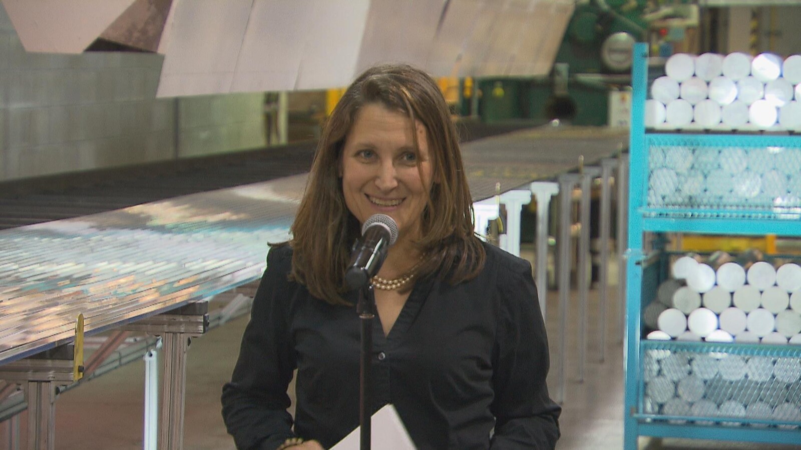 Chrystia Freeland se trouve derrière un microphone et elle affiche un air satisfait.