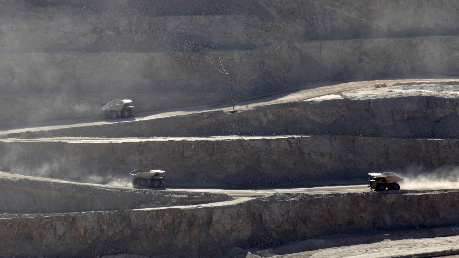 Des camions suivent un chemin en serpentin pour descendre et remonter de la mine.