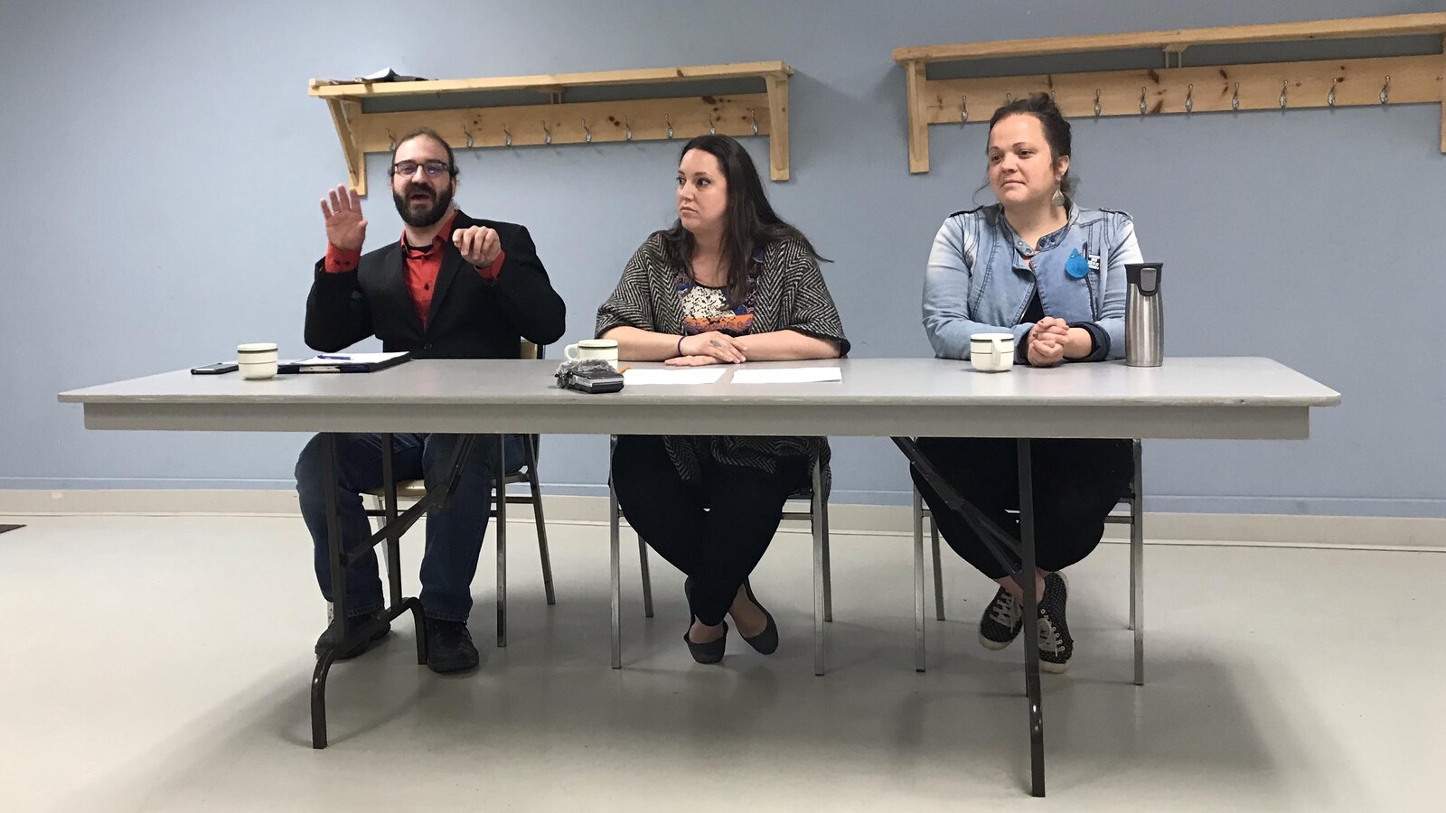 Un homme et deux femmes sont assis derrière une table durant un point de presse.