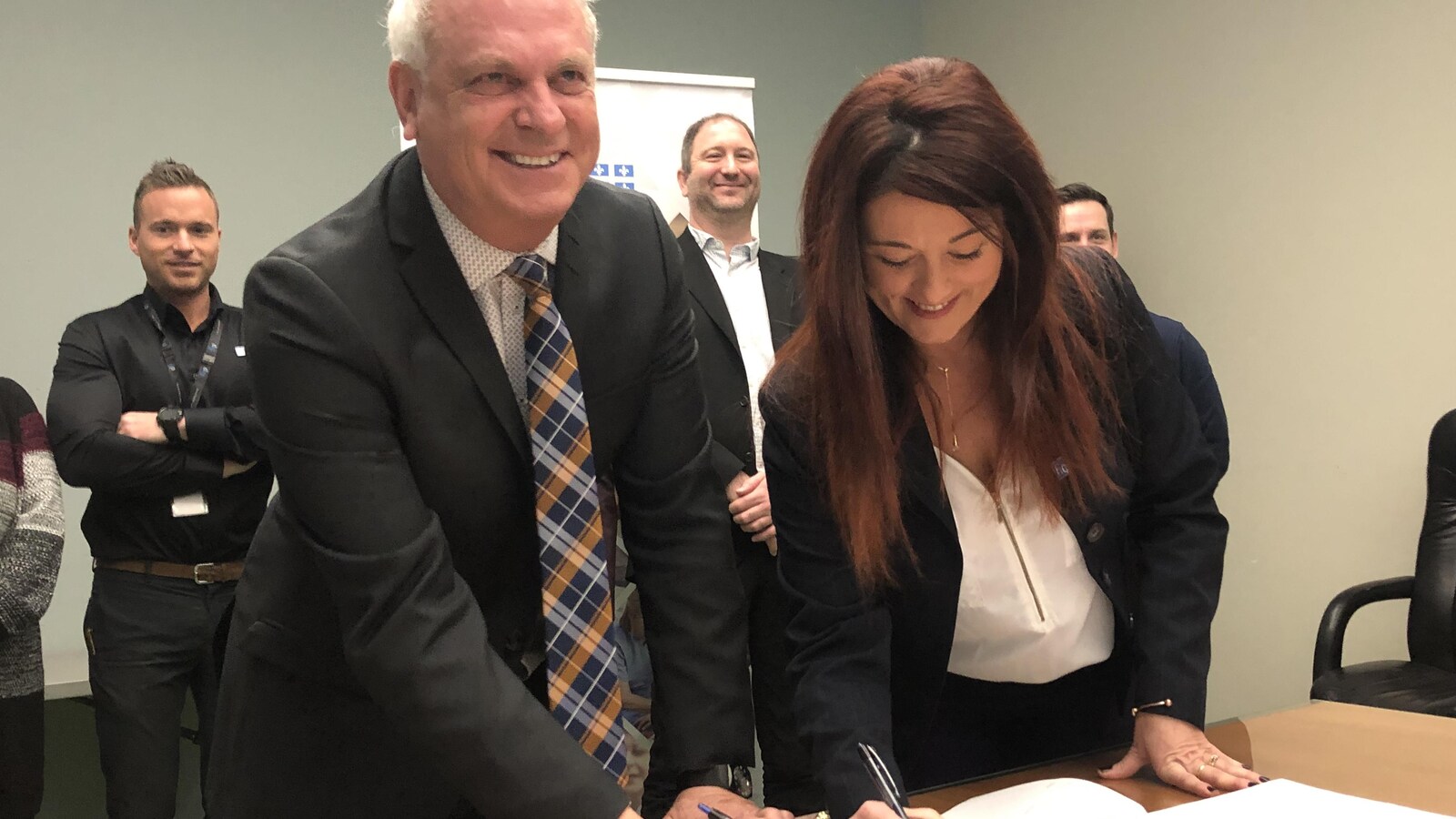 Louis Brunelle et Nathalie Perron tiennent chacun un crayon dans leur main et signent un document.