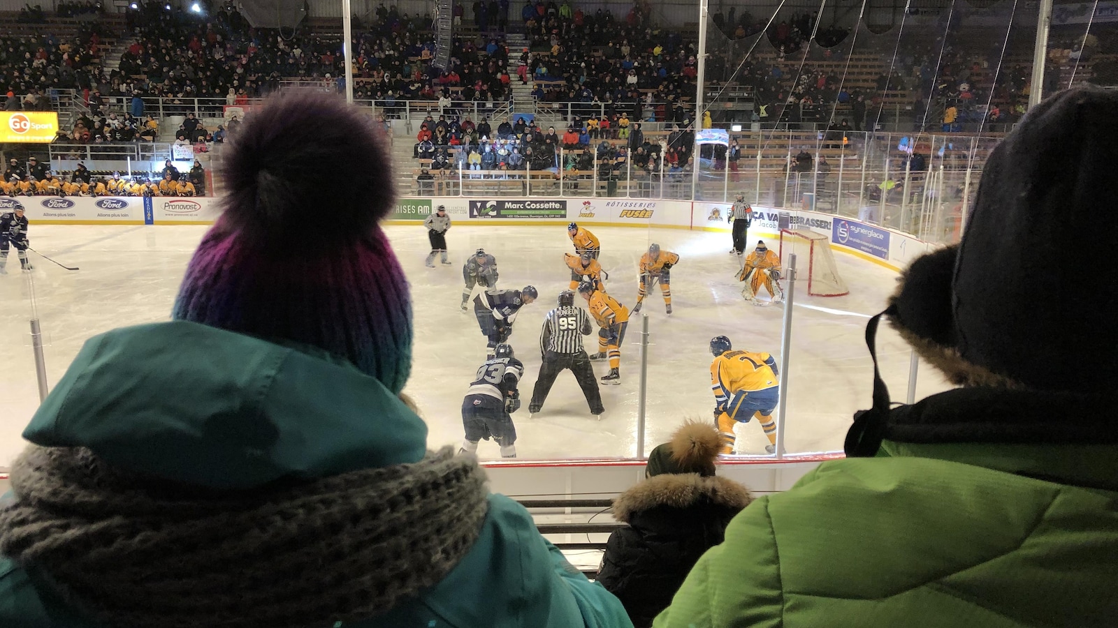 Des partisans regardent une patinoire alors que des joueurs de hockey procèdent à une mise au jeu.