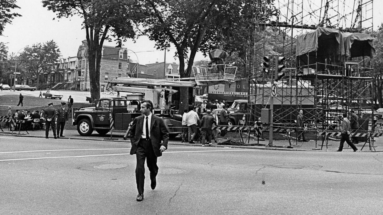 Claude Jean Devirieux, marchant devant les installations de Radio-Canada en prévision du défilé, dont une tour d'éclairage, un car de reportage et plusieurs barrières de sécurité.