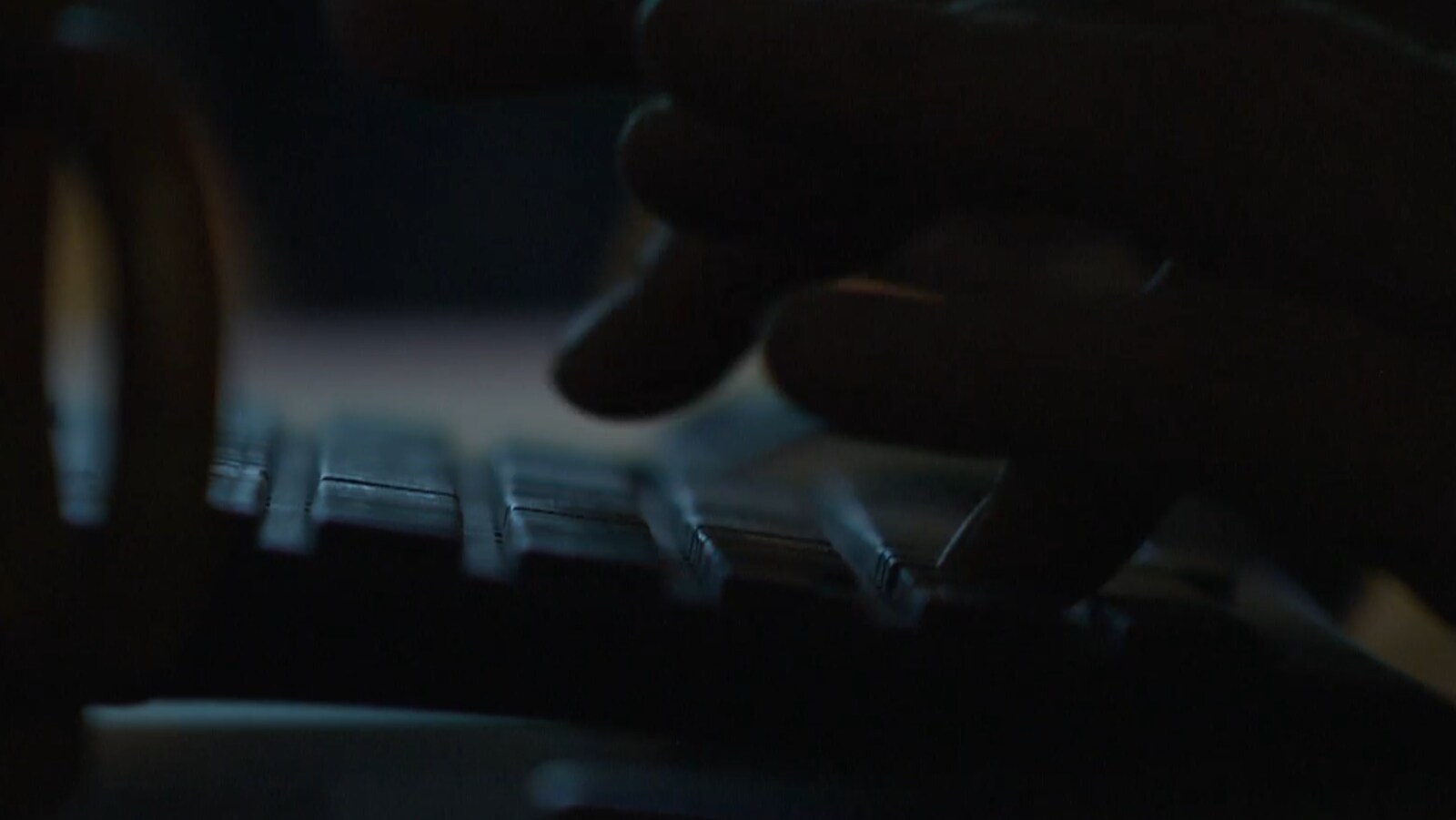 Des doigts tapent sur un clavier dans une pièce sombre.
