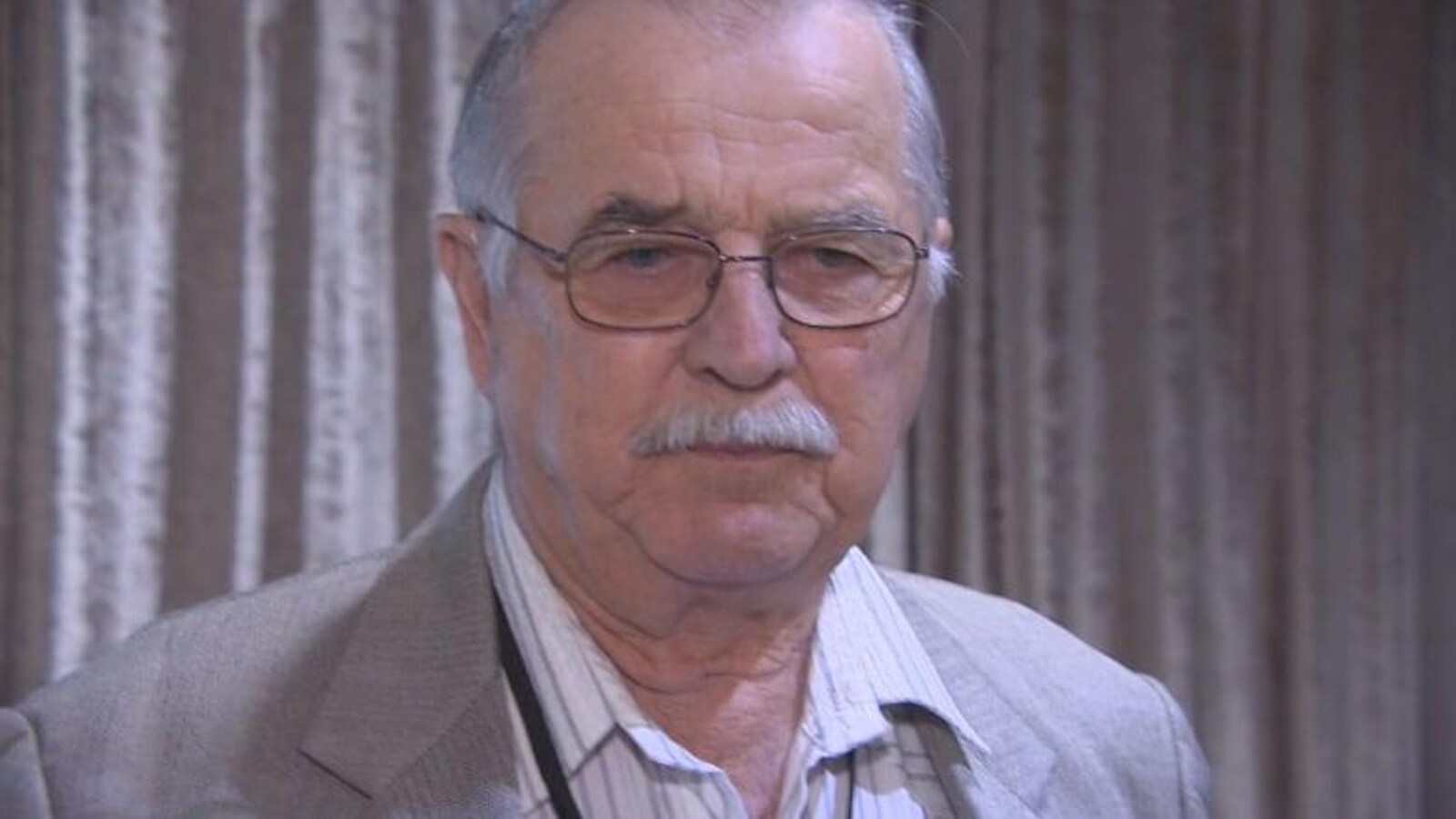 Portrait d'un homme aux cheveux et à la moustache gris, qui porte des lunettes.
