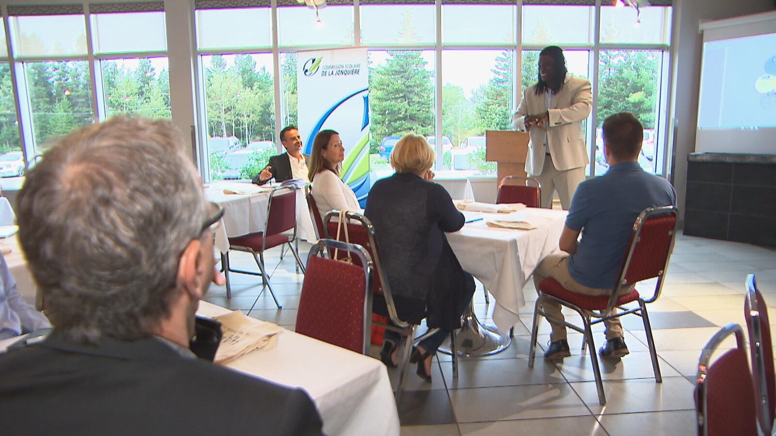 Un homme parle devant des personnes de la commission scolaire.