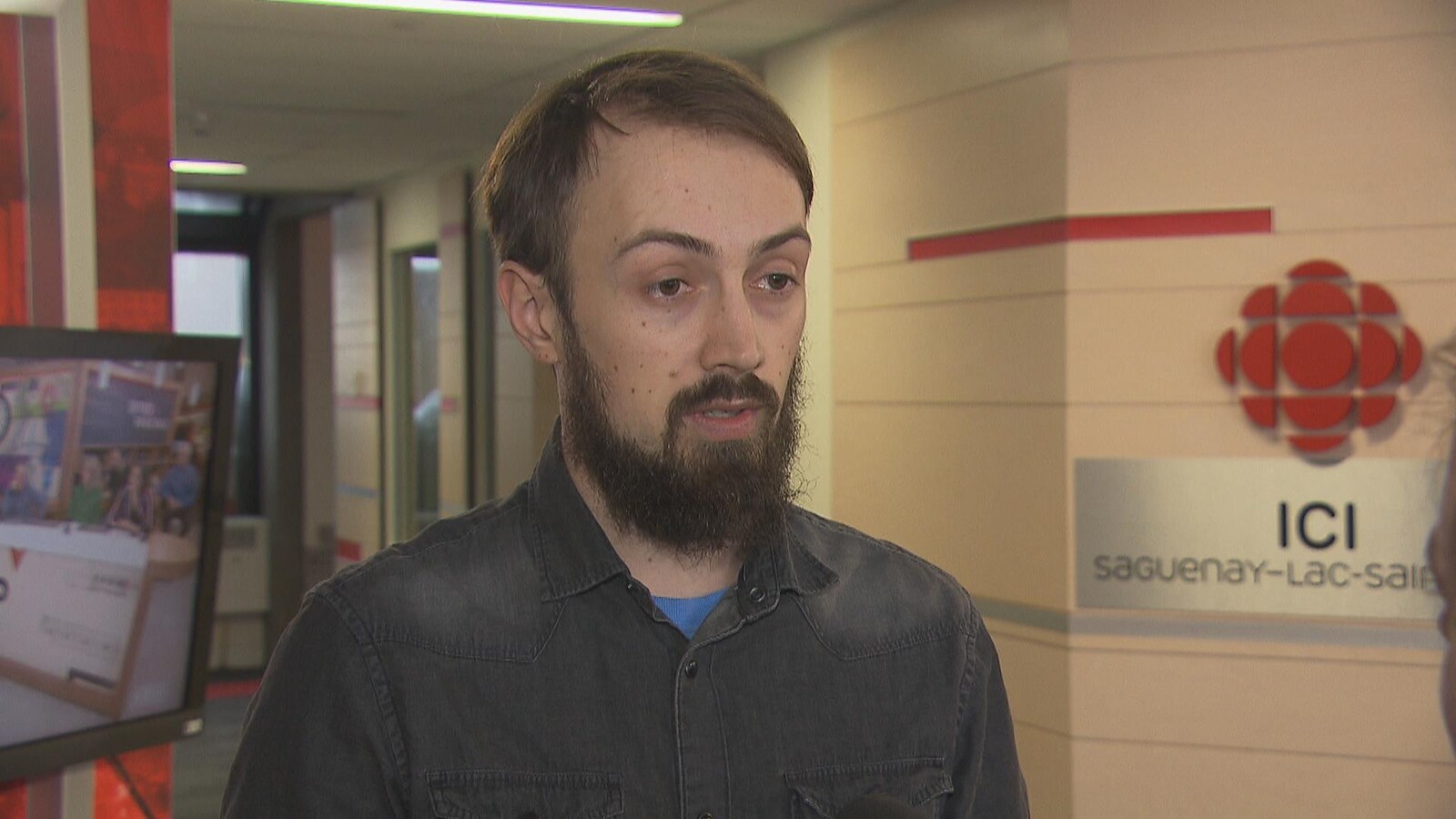 Homme barbu debout devant le logo de Radio-Canada en entrevue