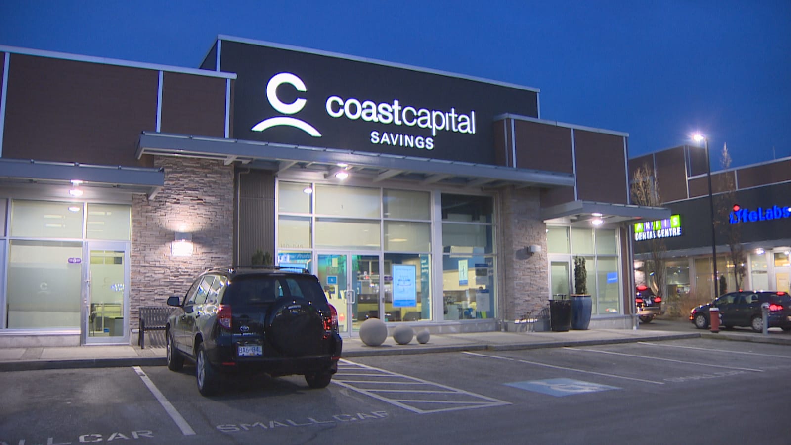 Plan large d'une des succursales de Coast Capital, vue de l'extérieur, en soirée, avec une voiture stationnée devant.