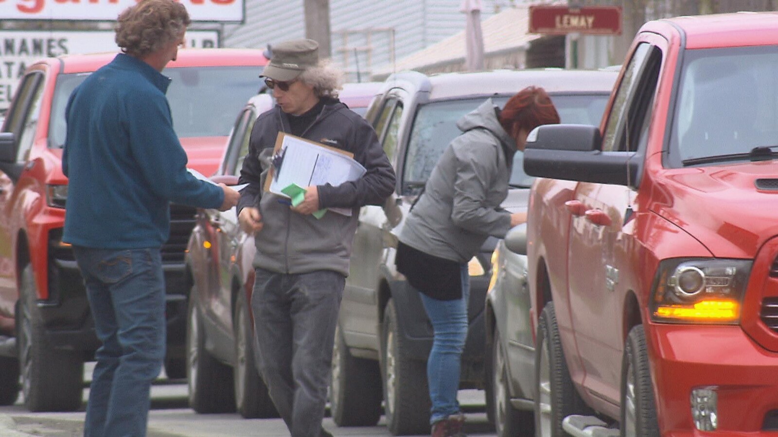 Trois personnes accostent des gens dans leur automobile pour leur faire signer une pétition.