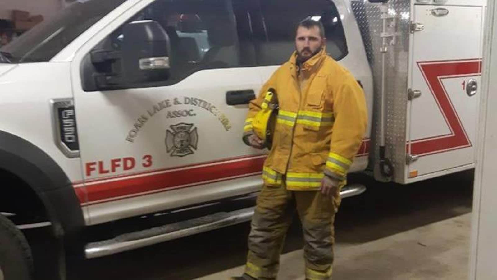 Le pompier bénévole Cole Maksymytz tient son casque sous le bras devant une ambulance.