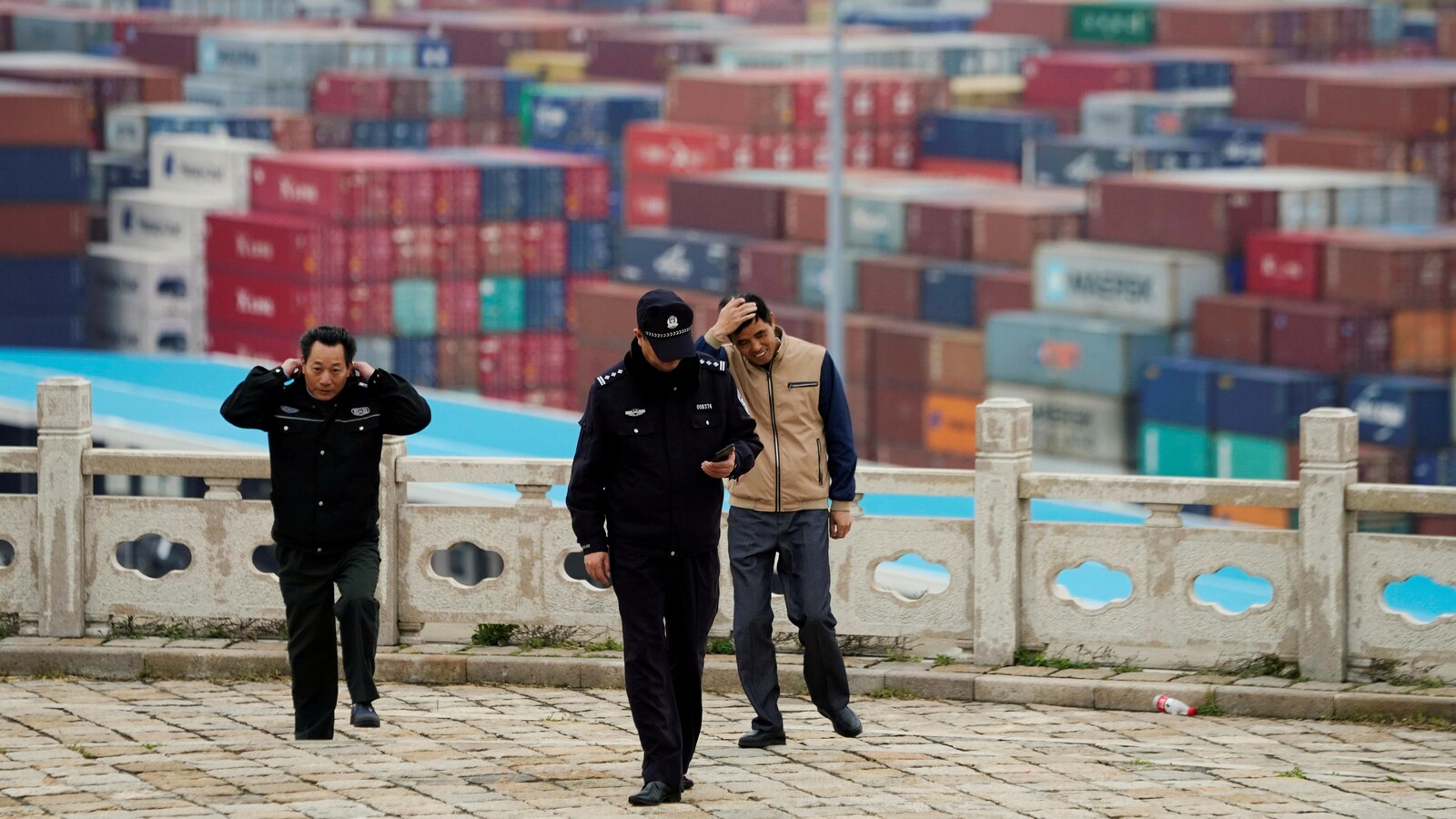 Des gardiens de sécurité marchent dans un port. En arrière-plan, des centaines de conteneurs.