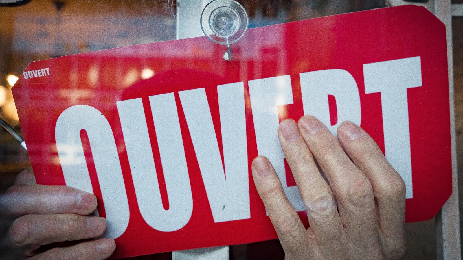 Des mains tournent une pancarte pour indiquer que le magasin est ouvert
