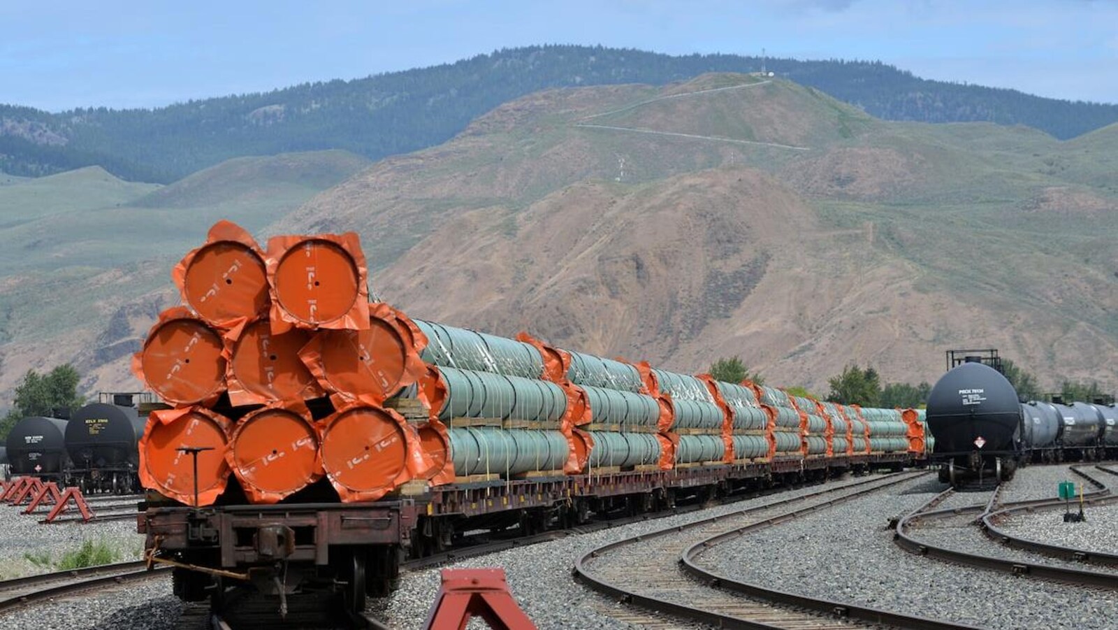 Des conduites sont sur des wagons sur des rails devant des montagnes.