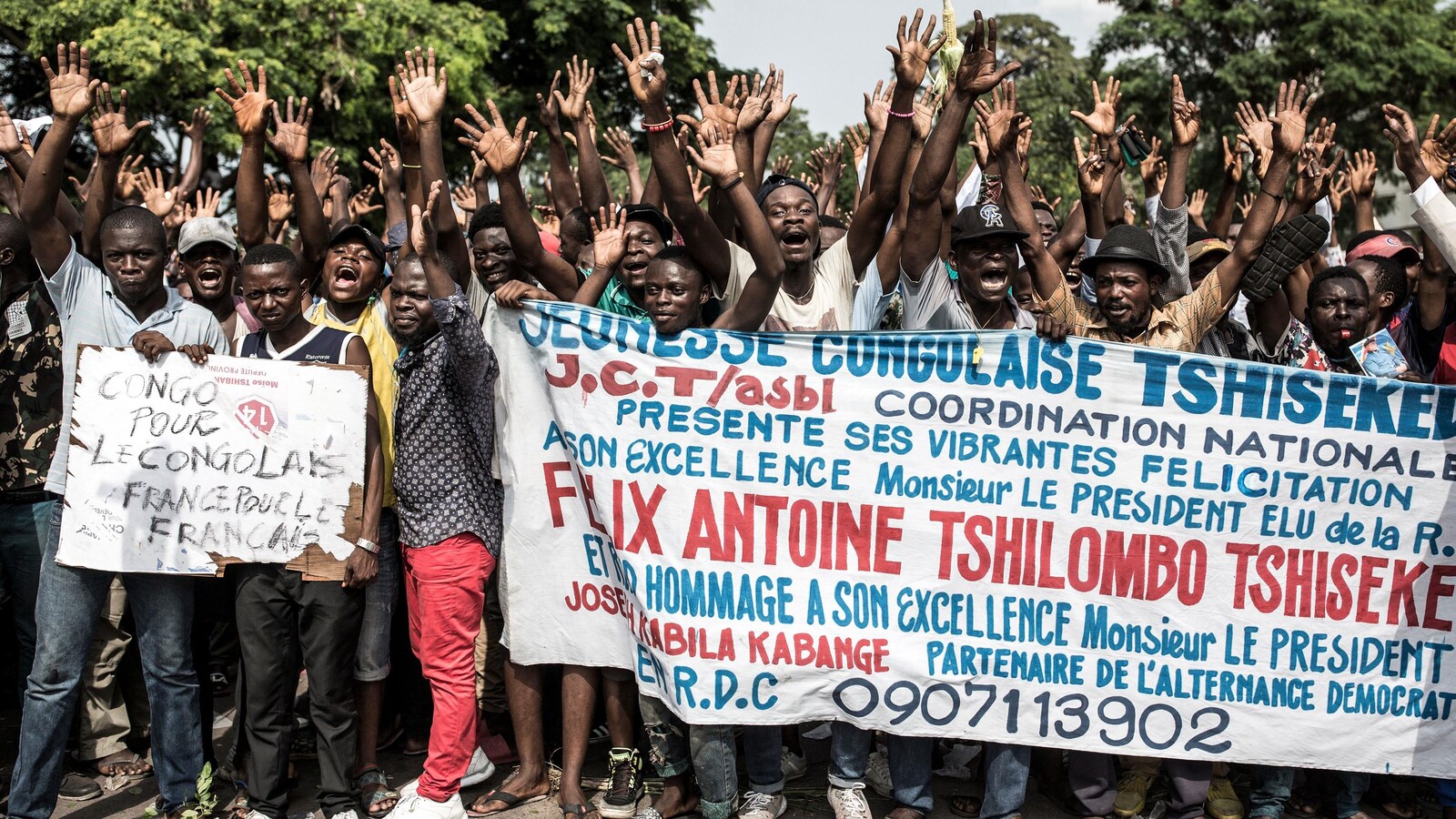 Des Congolais lèvent les bras en l'air tout en tenant une banderole dans une rue de Kinshasa.