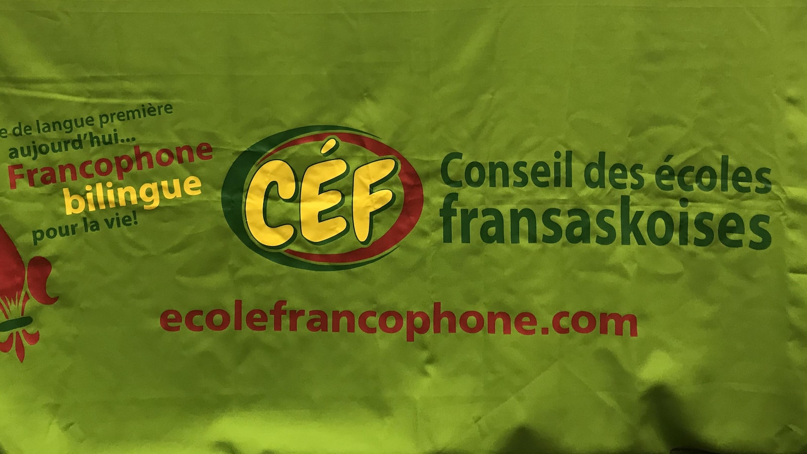 Une table aux couleurs du Conseil des écoles fransaskoises, avec le logo jaune et vert et rouge, ainsi que des éléments sur la table, comme une balance et un projecteur