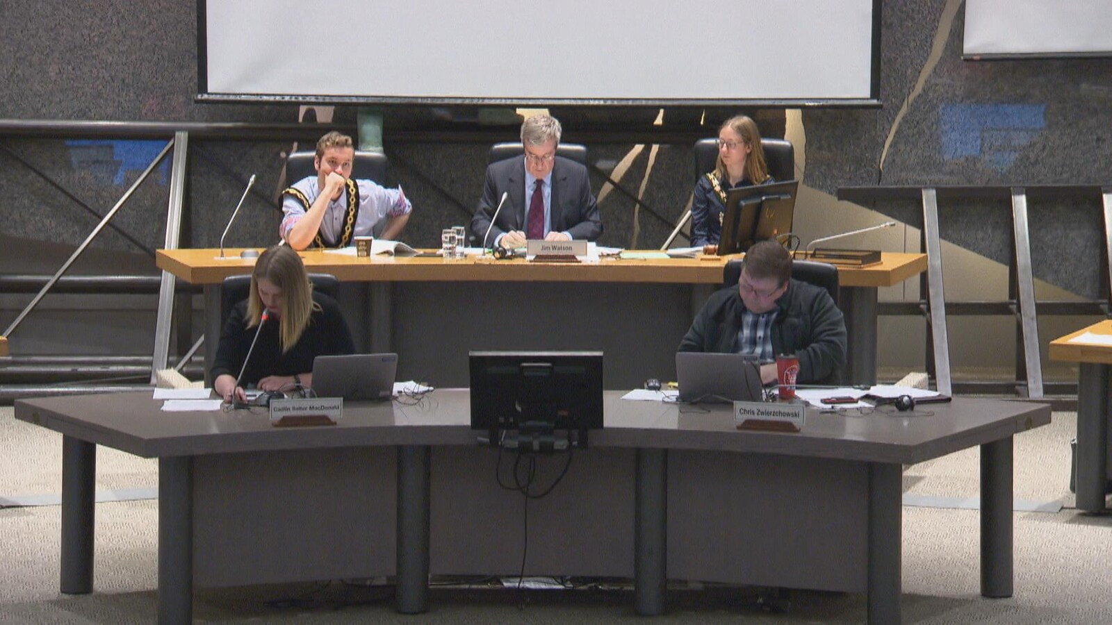 Cinq personnes assises à une table qui regardent des feuilles ou des ordinateurs