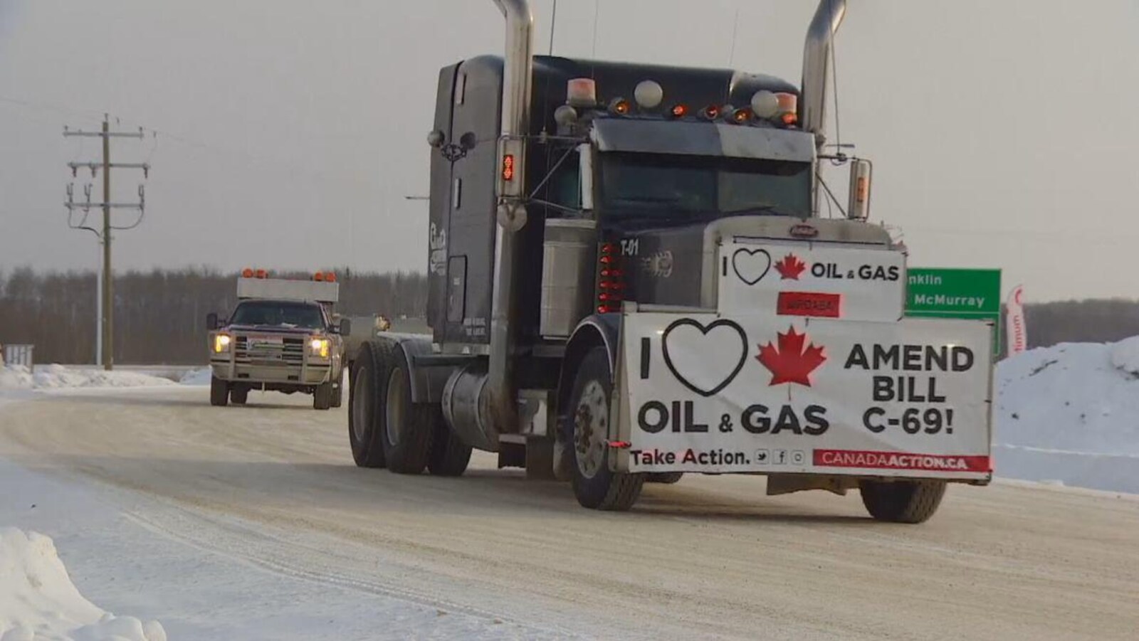 Un camion circule sur une route enneigée avec une bannière indiquant une opposition au projet de loi C-69.