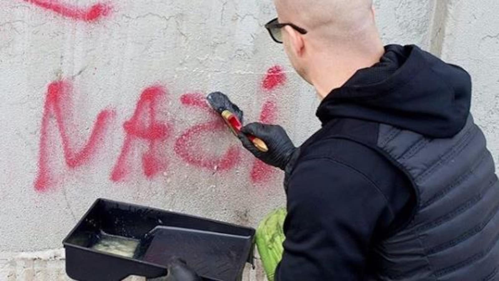 Un homme applique un produit liquide sur un graffiti antisémite afin de l'effacer.