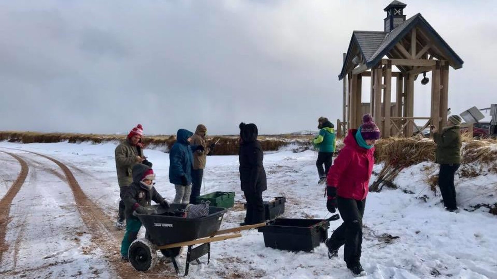 Un groupe de Madelinots ramassent des déchets sur une plage à l'aide de bacs et d'une brouette.