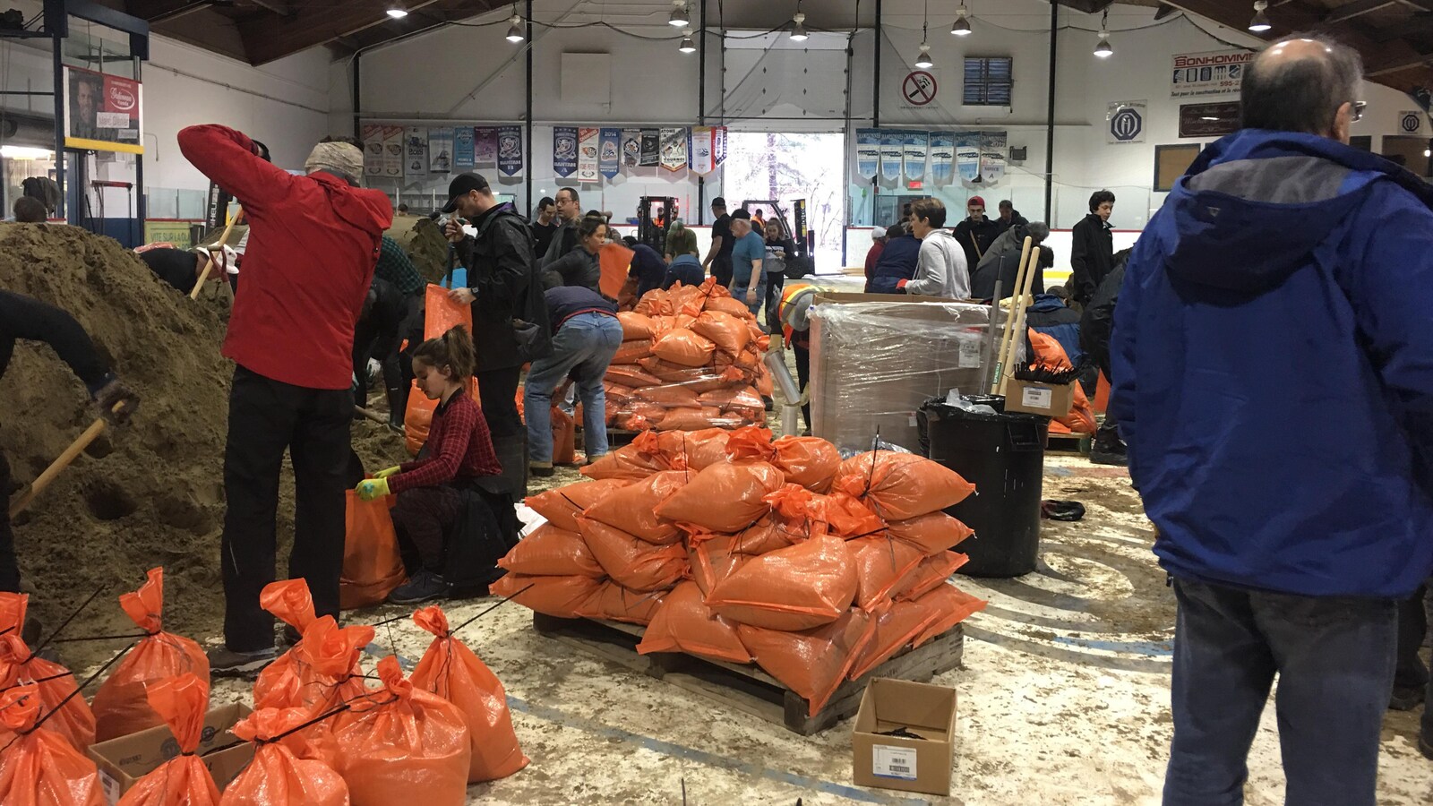 Des sacs oranges remplis de sable avec des bénévoles qui les remplissent