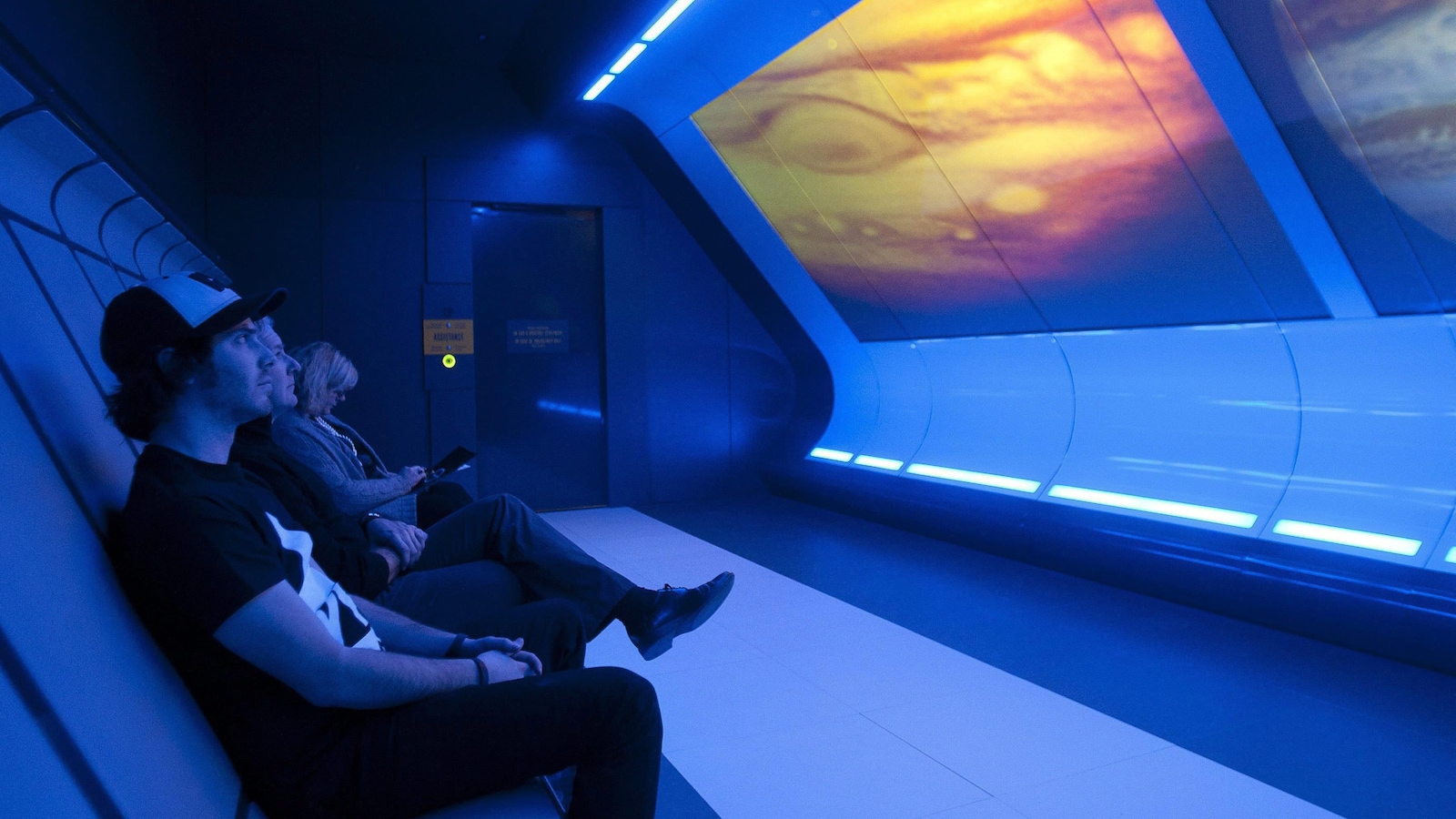 Trois personnes regardent une exposition sur le Cosmo.