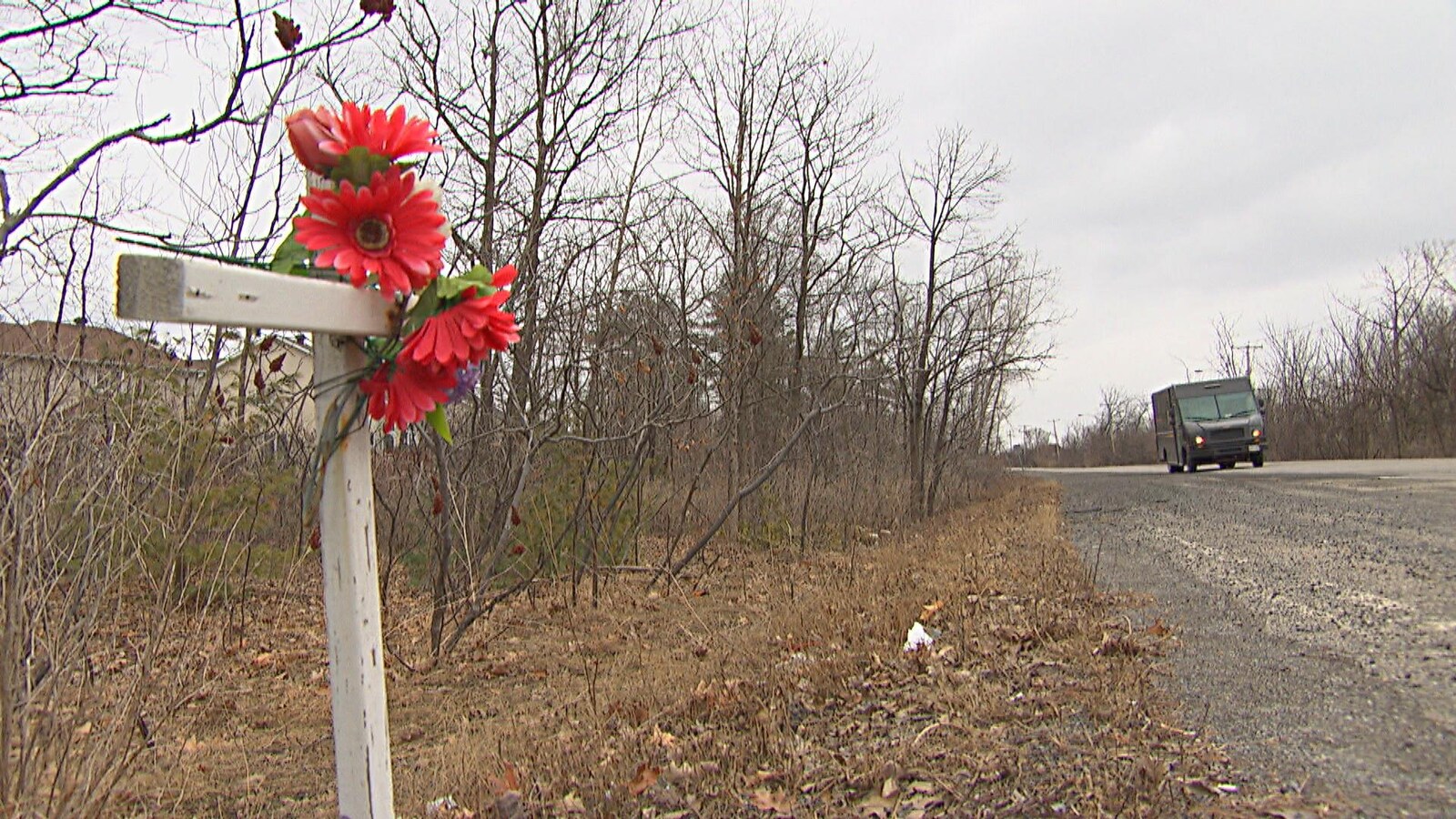 Une croix décorée de fleurs rouges posée en bordure d'une route.