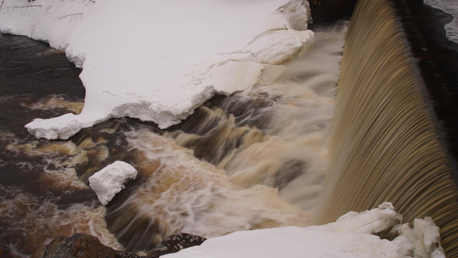 L'eau d'un barrage qui coule, entourée de neige.