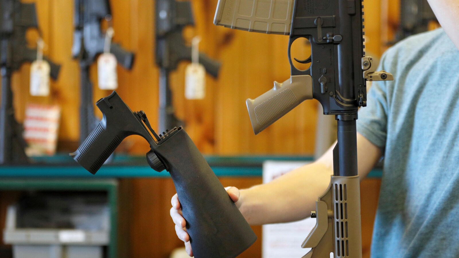Un vendeur tient une crosse avec accélérateur de tir sur un comptoir, où est déposée une arme semi-automatique.