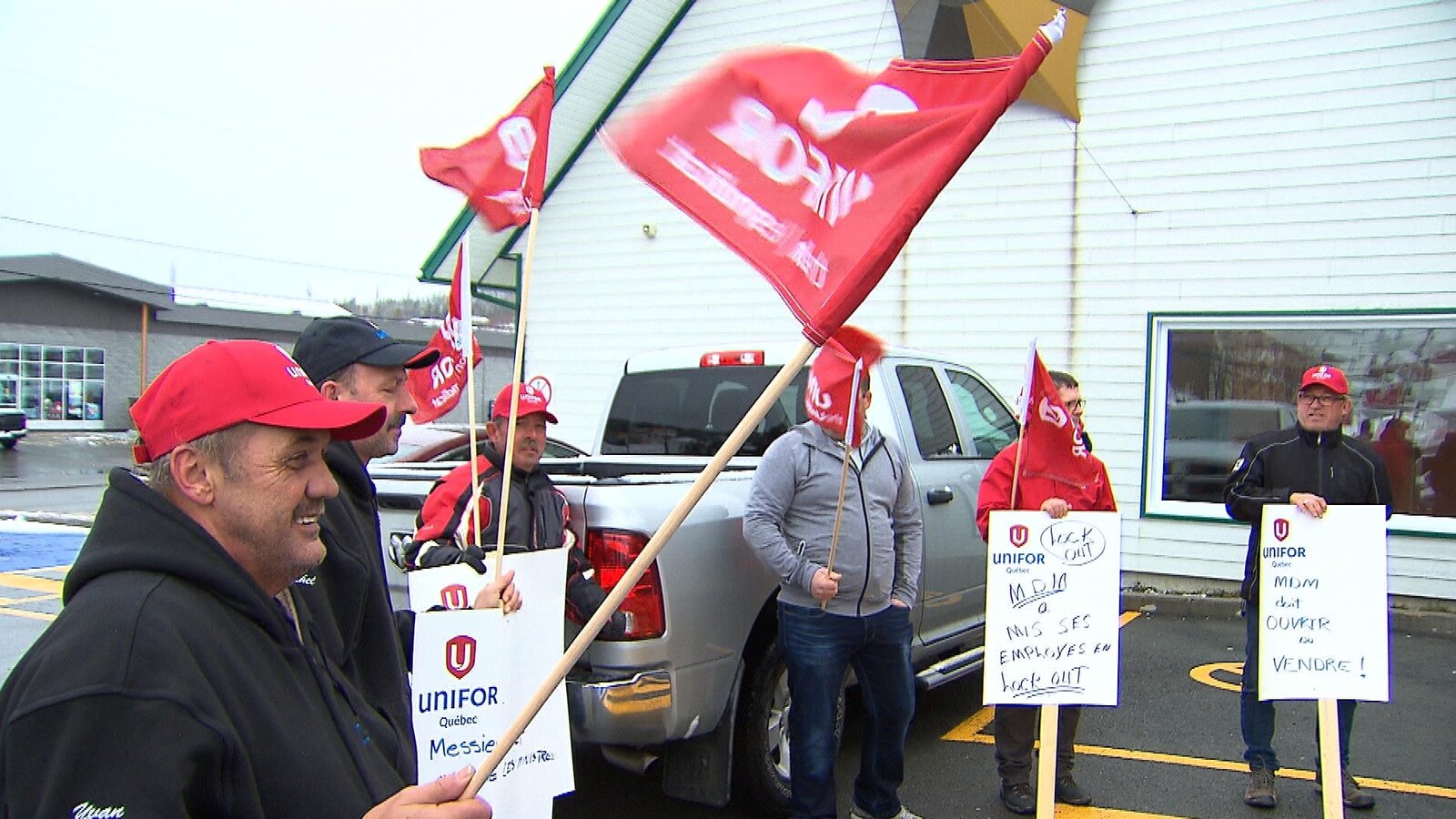 Des manifestants avec différentes pancartes et des drapeaux rouges avec le logo d'Unifor