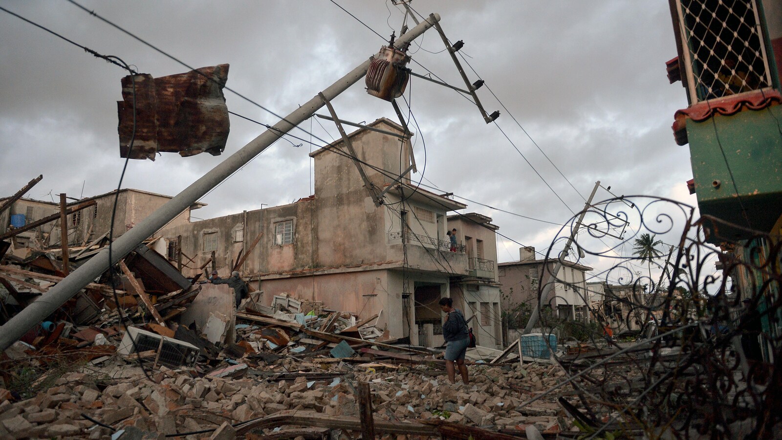 Une femme se déplace dans les débris de plusieurs maisons sous un ciel nuageux.