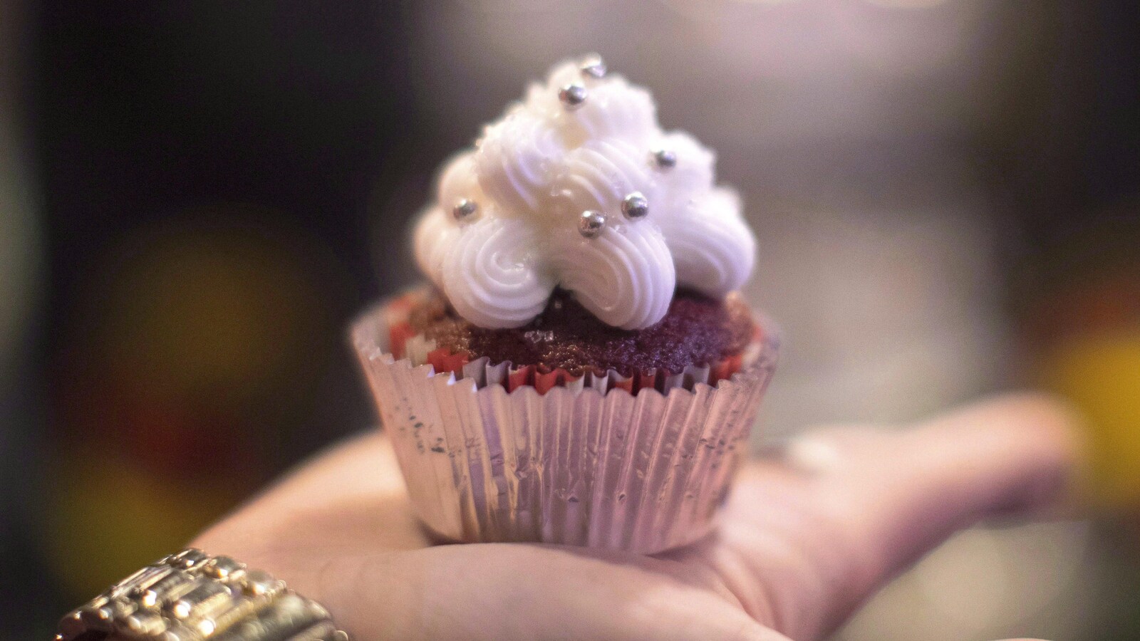 Un petit gâteau au cannabis placé dans un papier aluminium et décoré d'un glaçage à la vanille est dans la paume d'une main.