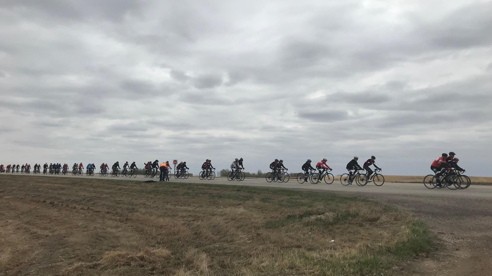La photo est prise dans un champ, au loin on voit la longue file de vélo qui se suivent dans les prairies.