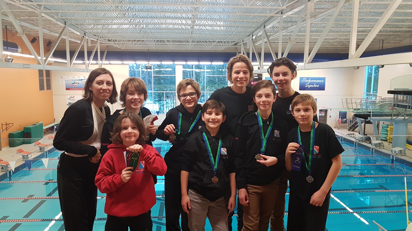 Des jeunes et leur entraîneuse posent avec leur médaille sur le bord d'une piscine de compétition.
