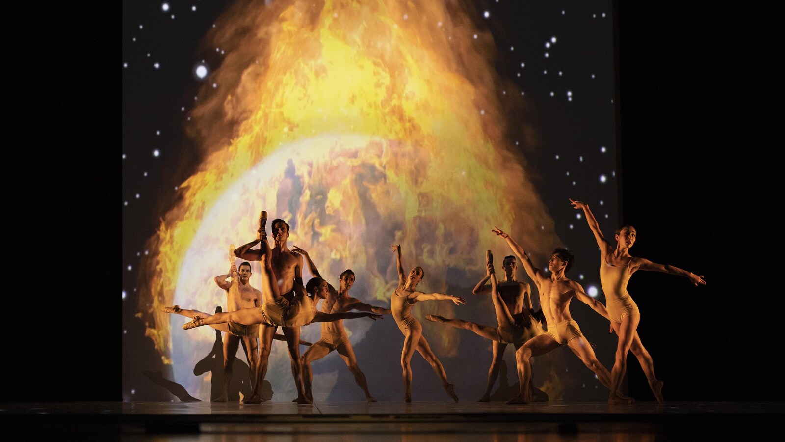 Des danseurs devant une planète en feu.