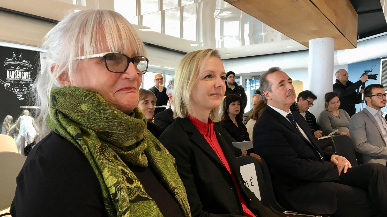 Deux femmes regardent une conférence de presse. L'une d'elle porte des lunette et un foulard.