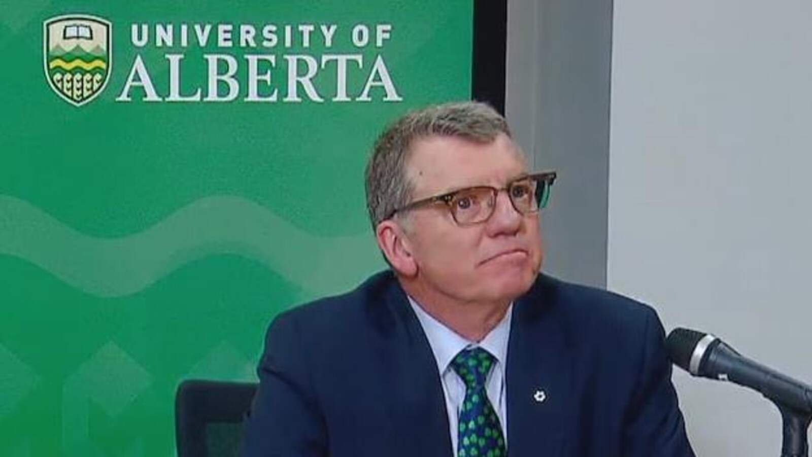 Le président de l'Université de l'Alberta, David Turpin, est assis en costume cravate devant un micro lors d'une conférence de presse.
