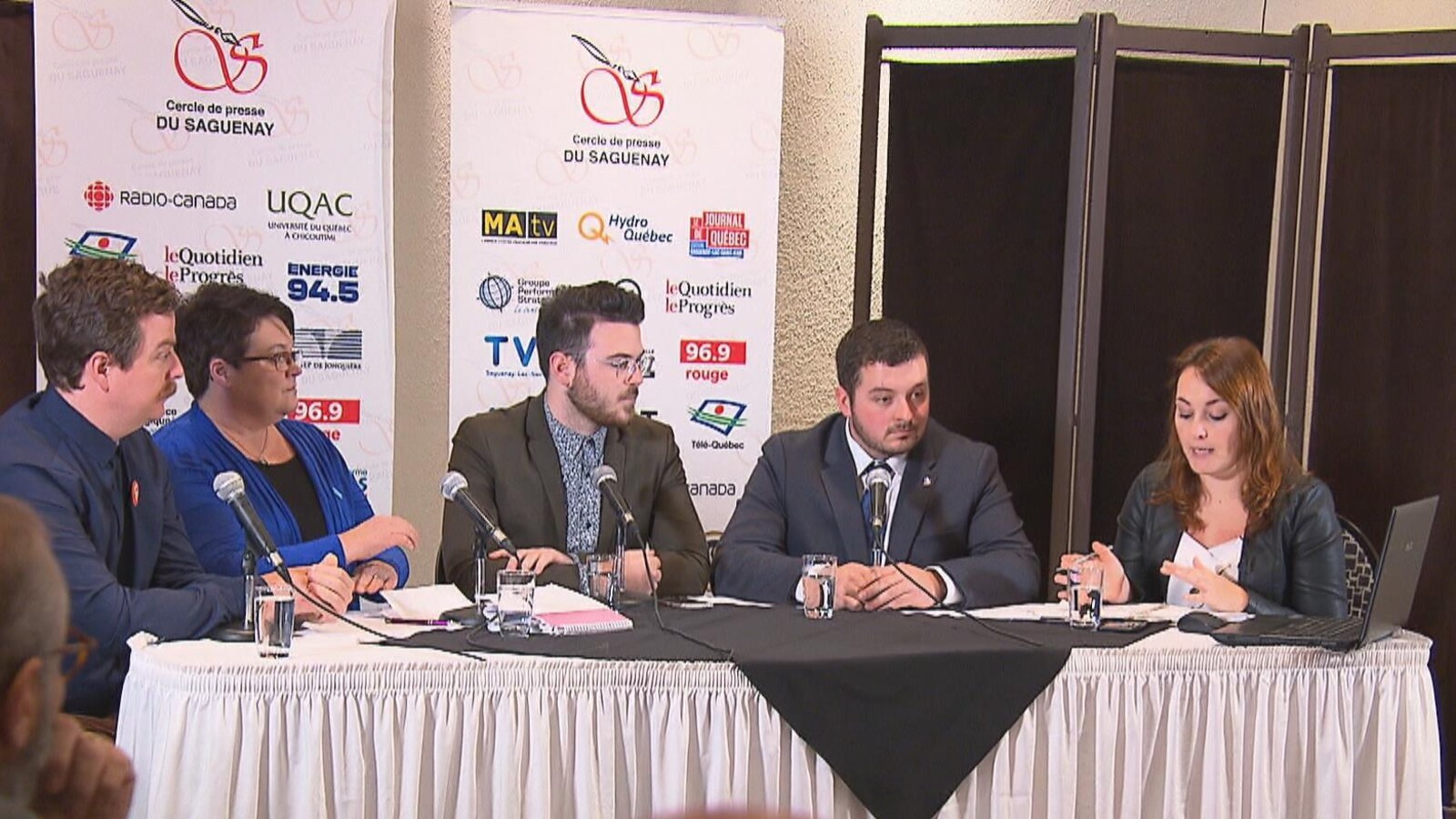 Cinq personnes sont assises à une table. Derrière, il y a deux affiches du Cercle de presse.