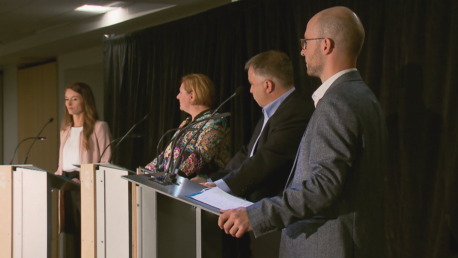 Les quatre participants au débat écoutent une question posée par l’animateur des échanges, le journaliste Pierre Jobin. Les candidats se tiennent debout derrière un lutrin. On aperçoit, de gauche à droite : Joëlle Boutin, Diane Lavallée, Sébastien Proulx et Sol Zanetti.