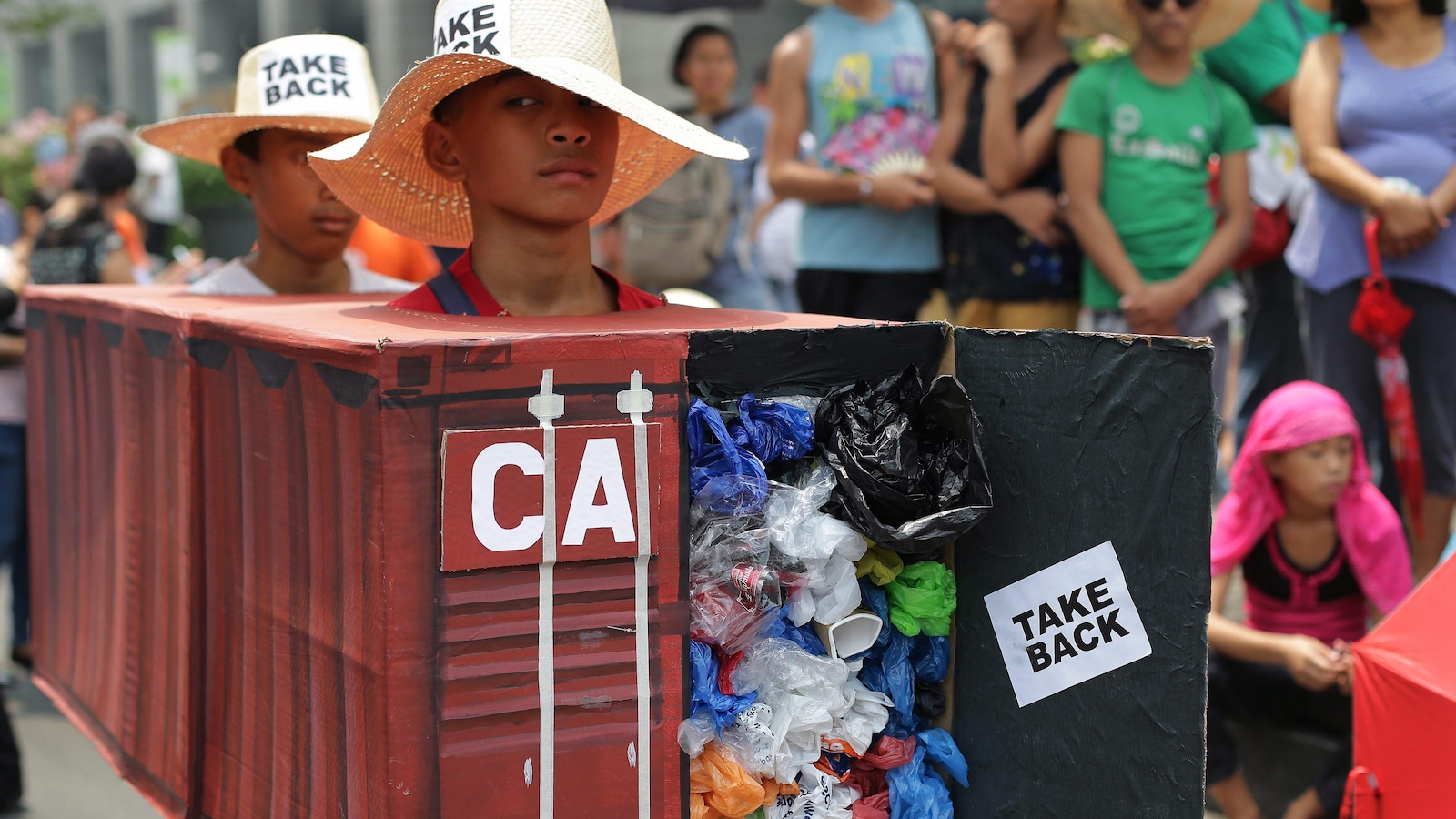 Un garçon déguisé en conteneur plein de déchets avec la mention «reprenez-les».