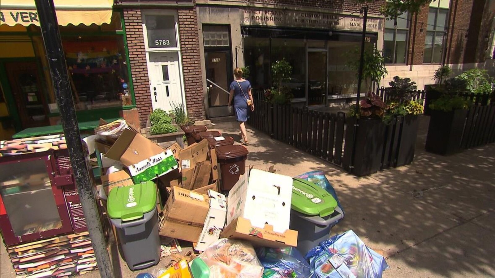 Des piles de boîtes en carton, de bacs verts et de bacs bruns en bordure de la rue.