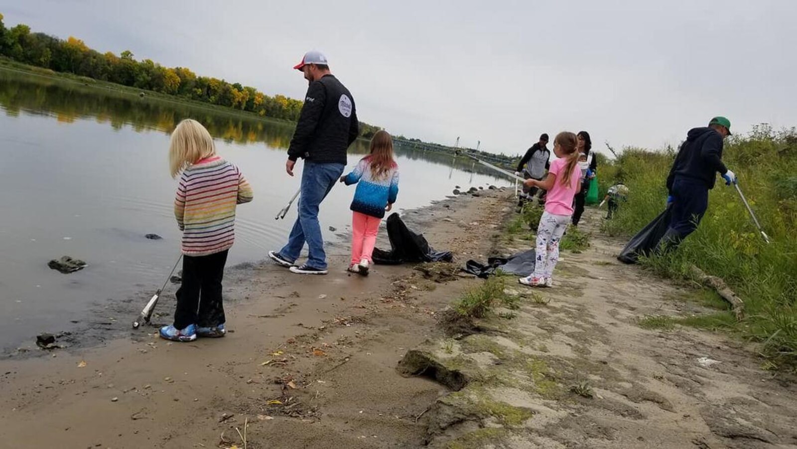 Trois enfants et un adulte au bord de la rivière Rouge ramassent des déchets